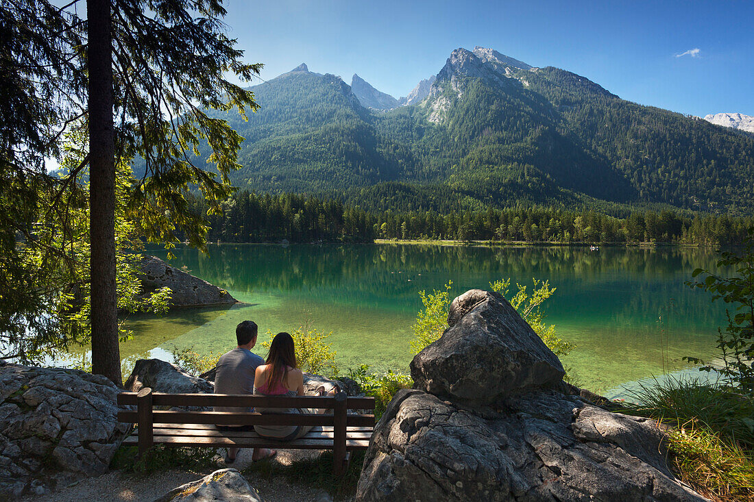 Junges Paar sitzt auf einer Bank am Hintersee mit Blick zum Hochkalter, Ramsau, Berchtesgadener Land, Nationalpark Berchtesgaden, Oberbayern, Bayern, Deutschland
