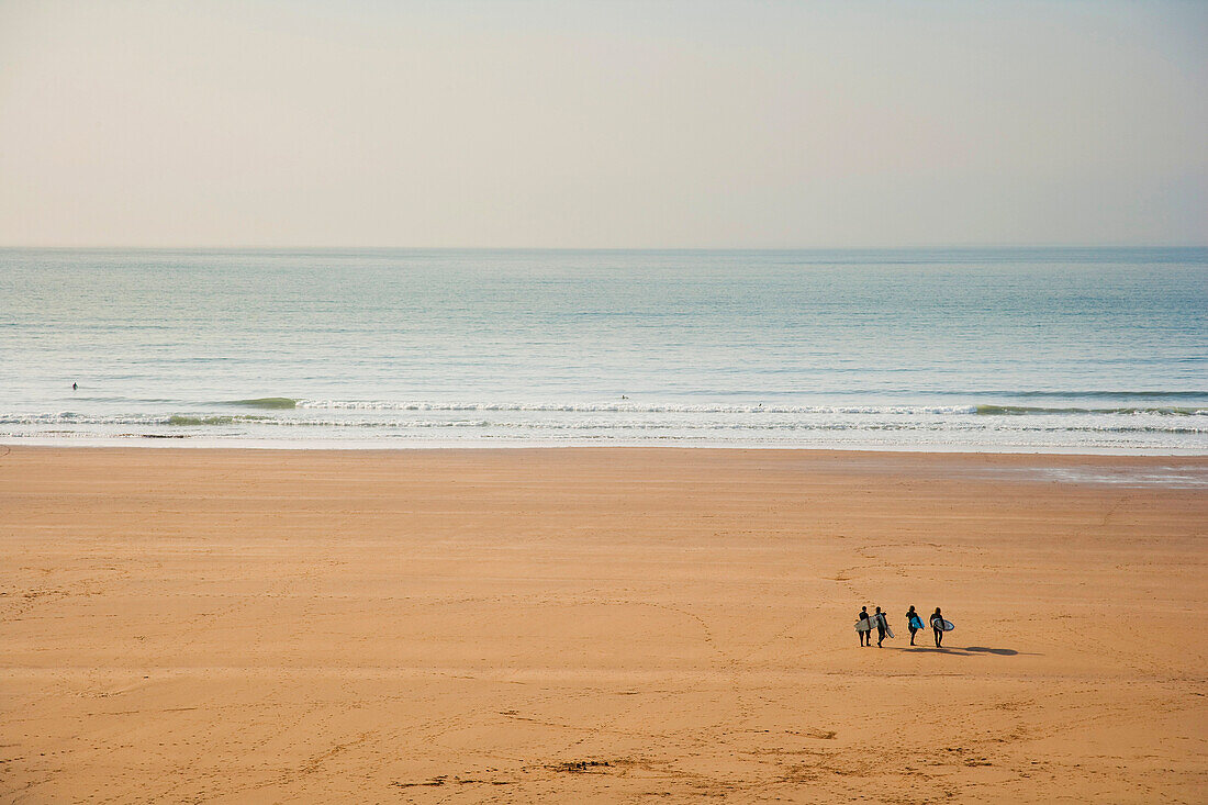 Group Of Surfers Walking On The Beach With Their Boards Towards The Sea In Putsborough Sands, North Devon, Uk