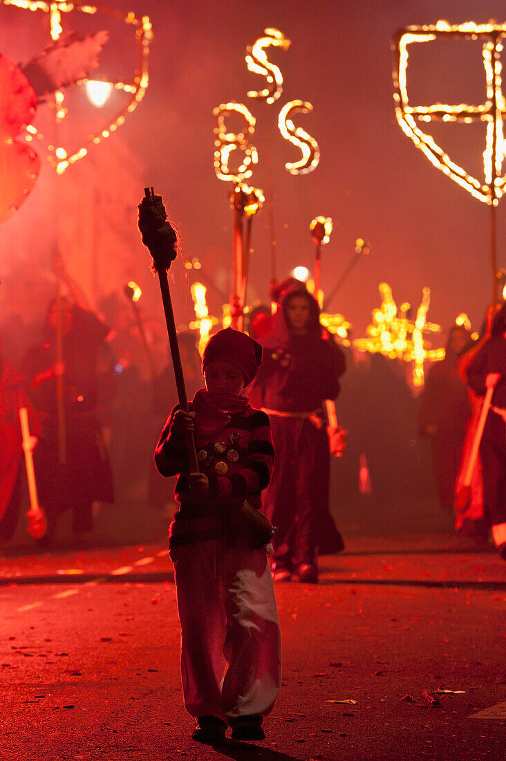 Young Boy Dressed As A Smuggler With Torch On The United Grand Procession In Front Of Monks With Banners And Burning Crosses, Bonfire Night, Lewes, East Sussex, Uk