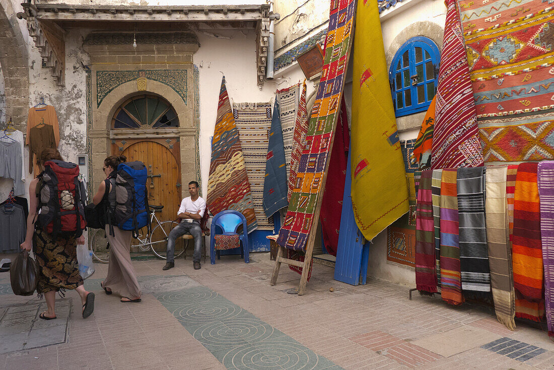Backpackers Wander Through Carpet Market In Essaouira, Morocco