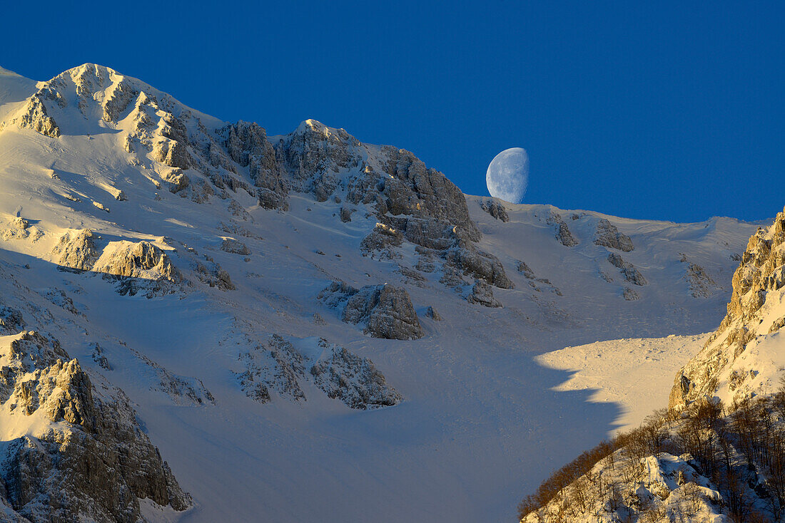 Moon standing above the snow-covered cirque at Monte Sirente, Valle Lupara, Monte Sirente, Abruzzi, Apennines, l' Aquila, Italy
