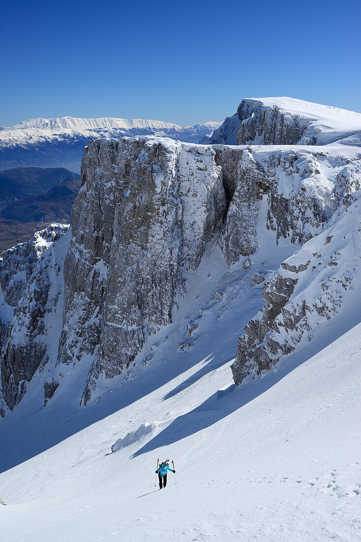 Female backcountry skier ascending through snow-covered cirque at Monte Sirente, Maiella range in background, Valle Lupara, Abruzzo, Italy