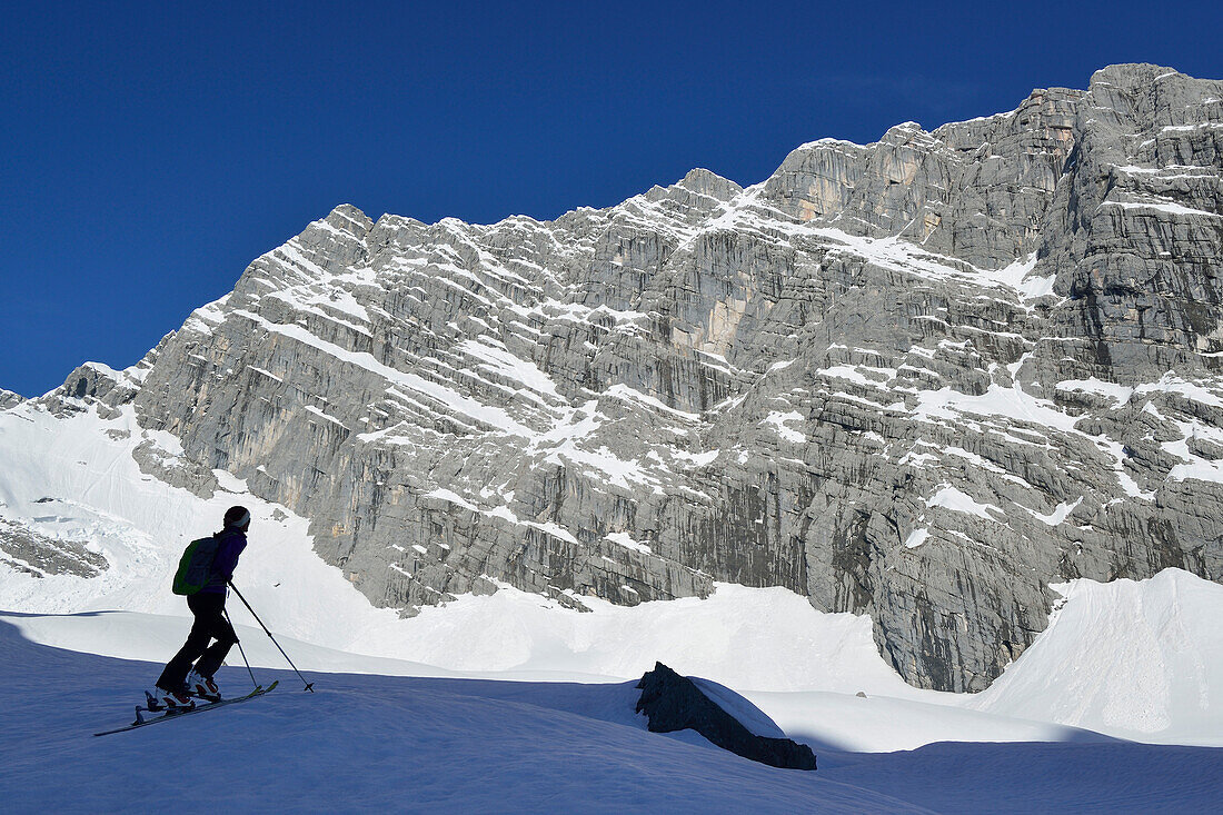 Female backcountry skier looking at Watzmann east wall, Watzmannkar, Berchtesgaden Alps, Berchtesgaden National Park, Upper Bavaria, Bavaria, Germany