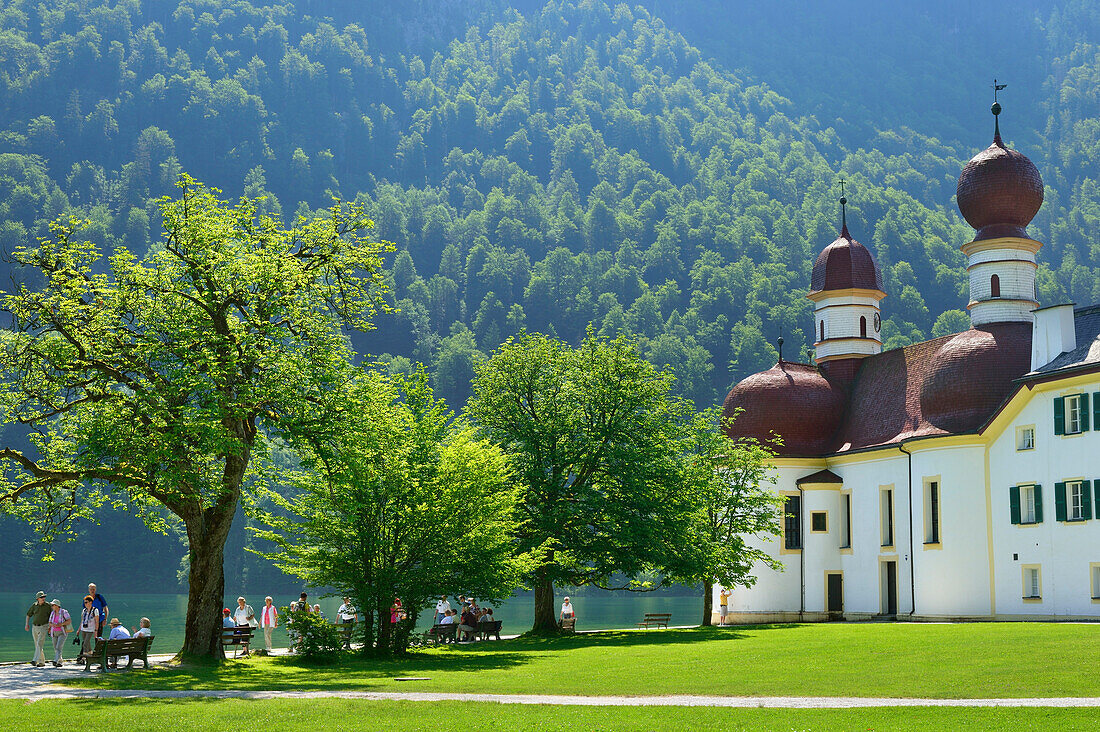 People walking along the promenade of lake Koenigssee with church of St. Bartholomae, St. Bartholomae, lake Koenigssee, Berchtesgaden range, National Park Berchtesgaden, Berchtesgaden, Upper Bavaria, Bavaria, Germany