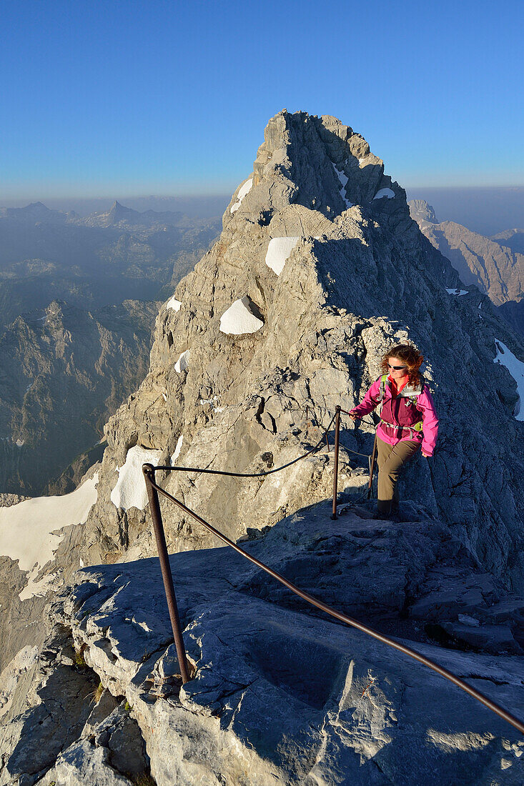 Woman ascending alongside fixed ropes to Watzmann, Watzmann ridge and Mittelspitze in background, Berchtesgaden Alps, Berchtesgaden National Park, Berchtesgaden, Upper Bavaria, Bavaria, Germany