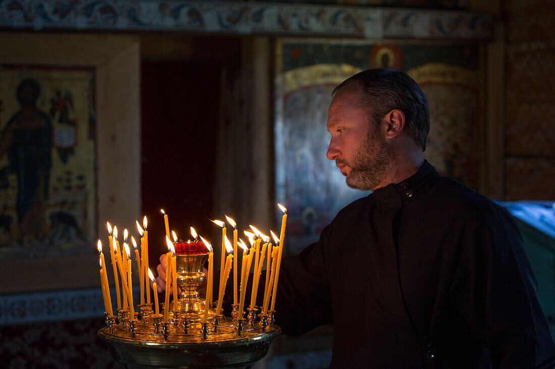 Priest with offering candles inside the Church of the Intercession of the Virgin at Kizhi Pogost, Kizhi Island, Lake Onega, Russia, Europe