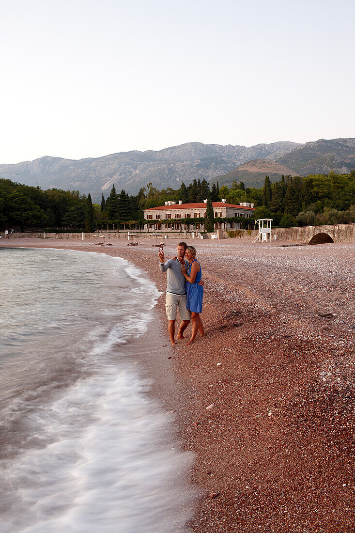 Paar am Strand im Abendlicht, Villa Milocer im Hintergrund, Aman Sveti Stefan, Sveti Stefan, Budva, Montenegro