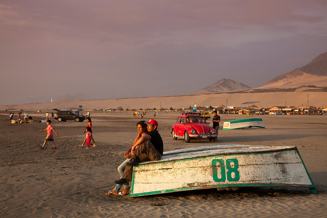 Ein paar sitzt auf einem Fischerboot am Strand und blickt in den Sonnenuntergang, Salaverry nahe Trujillo, La Libertad, Peru, Südamerika