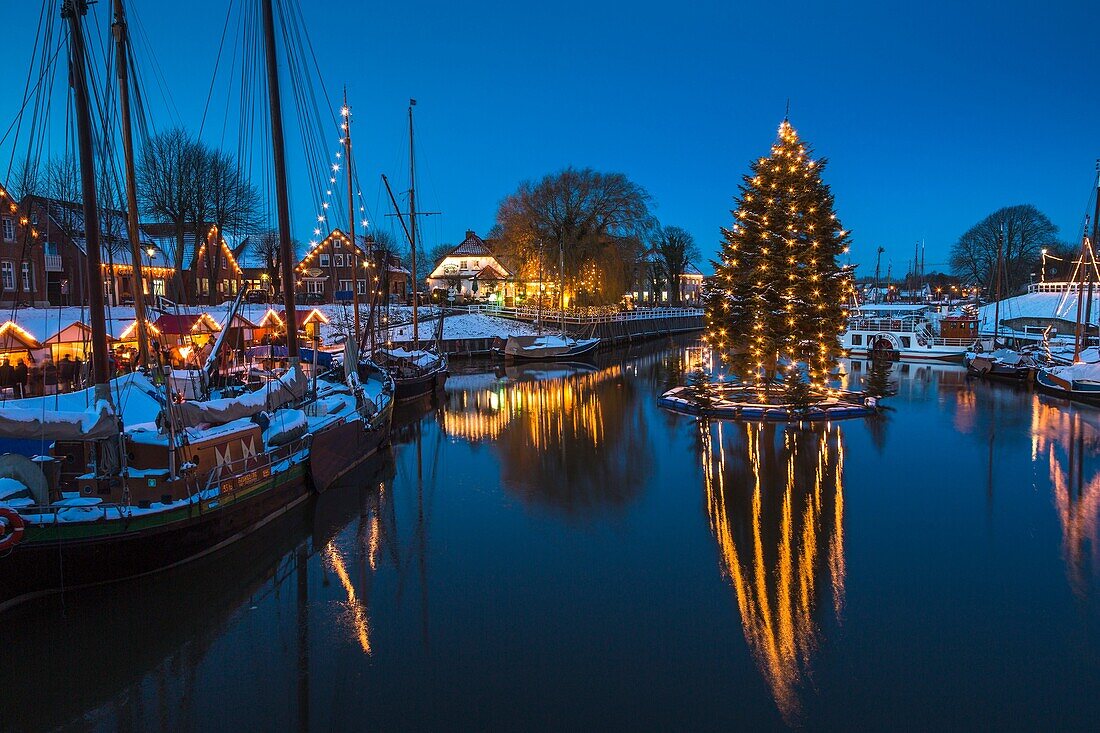 Floating christmas tree and vintage boats in the old harbour of Carolinensiel at twilight, Lower Saxony, Germany, Europe