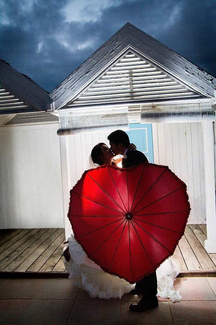 Wedding couple kissing with a red umbrella Ostia Rome Italy