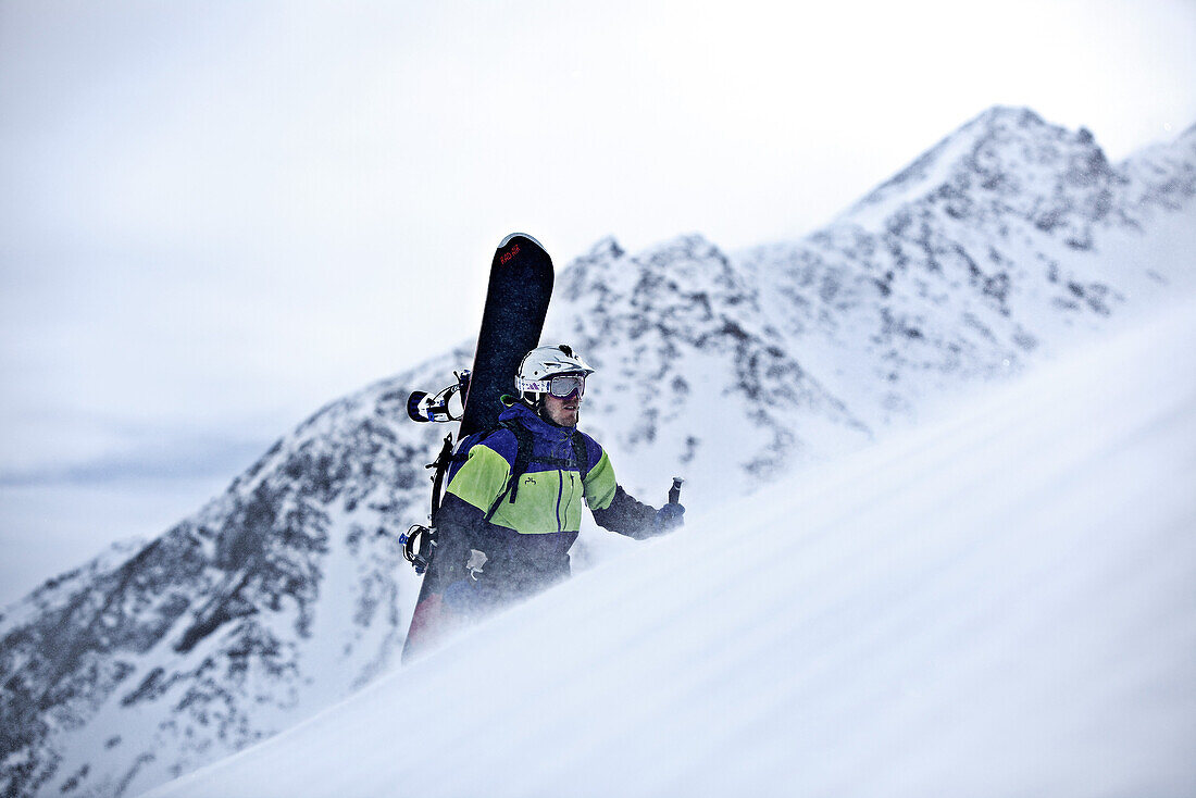 Junger Snowboarder steigt durch den Schnee in den Bergen, Pitztal, Tirol, Österreich