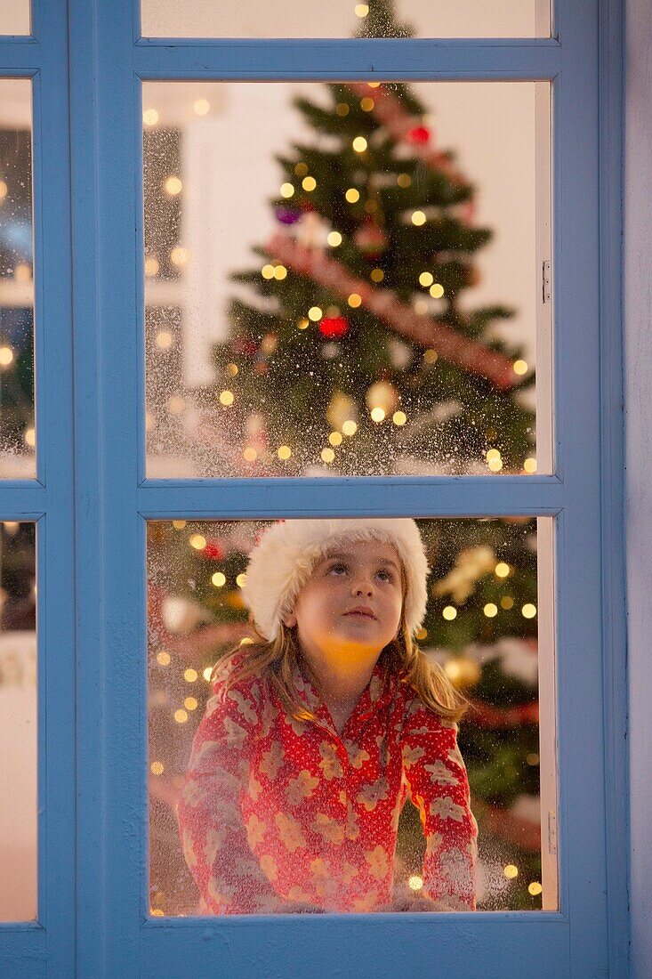 Junges Mädchen schaut aus dem Fenster und wartet auf den Weihnachtsmann