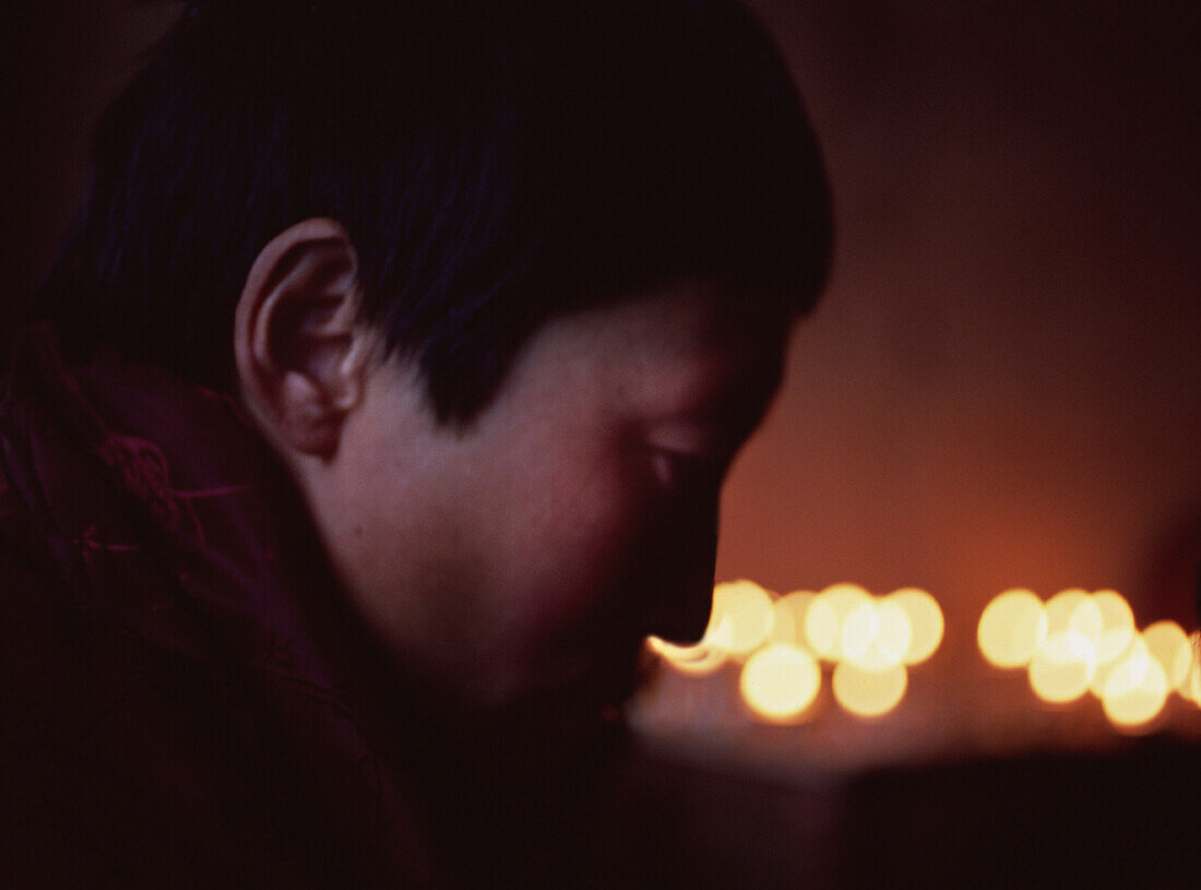 Tibetan Nun Praying with Candles in Background, Nangchen, Eastern Tibet