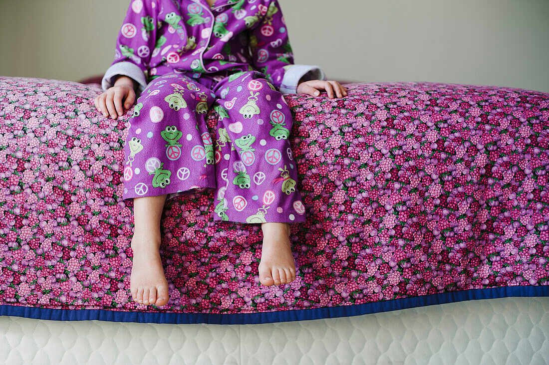 Young Girl in Purple Pajamas Sitting on Edge of Purple Bed