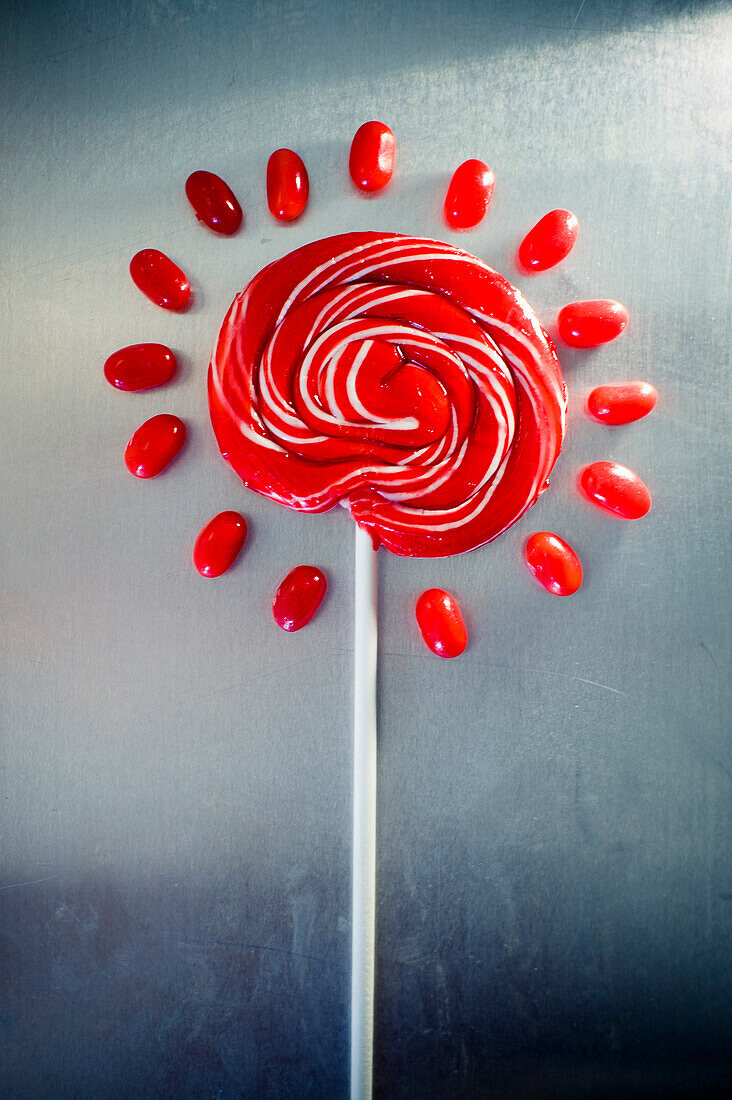 Red Lollipop Surrounded by Red Jellybeans on Metal Background