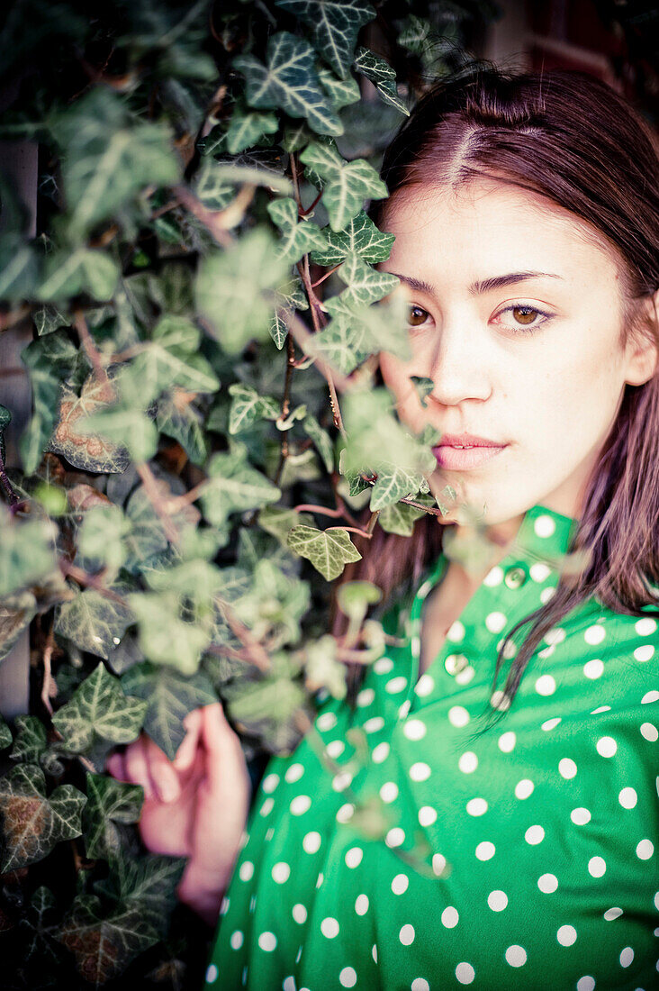 Serious Young Woman Peering Through Ivy