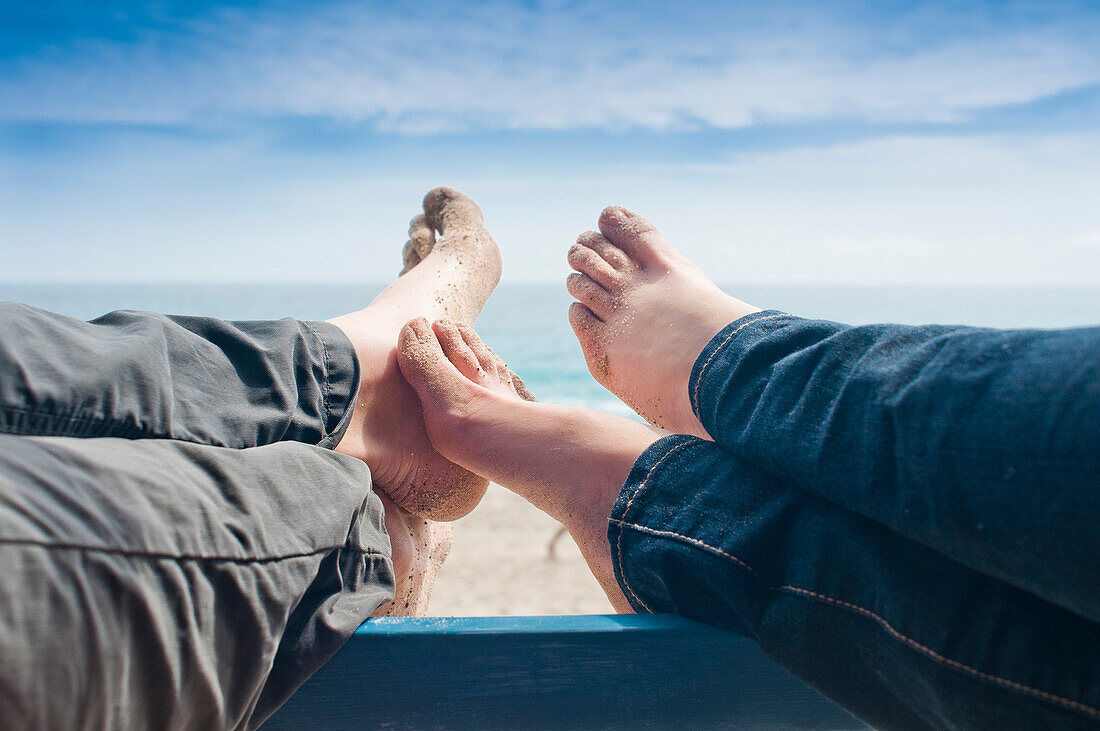 Couple's Sandy Bare Feet on Railing With Beach in Background