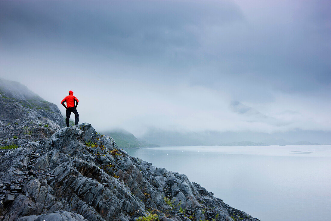A Lone Hiker Stands On A Rocky Outcropping Overlooking Shoup Bay On A Cloudy Day, Shoup Bay State Marine Park, Prince William Sound, Southcentral Alaska