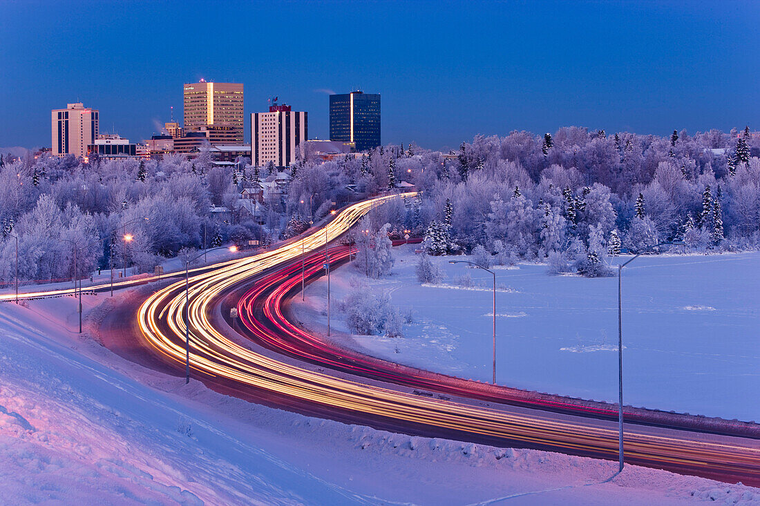 Alpenglow Over The Anchorage Skyline With The Lights From Traffic On Minnesota Blvd. In The Foreground During Winter, Southcentral Alaska