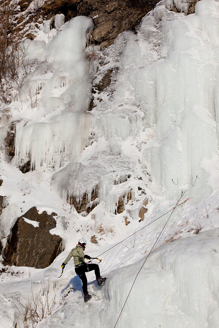 Female Ice Climber Rappels Down An Ice Wall Next To The Seward Highway, Southcentral Alaska, Winter