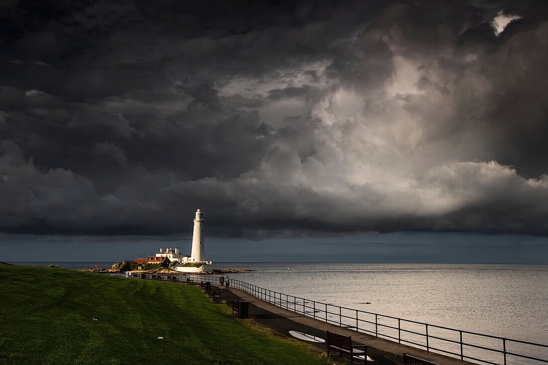 'White Lighthouse Illuminated By Sunlight Under Dark Storm Clouds; St. Mary's Island Northumberland England'