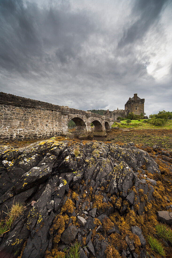 'An Old Stone Bridge Leading Towards Old Stone Buildings Under A Cloudy Sky; Kyle Of Lochalsh Scotland'
