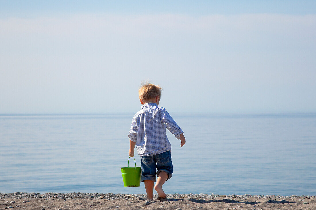 'Young Boy Carrying A Pail On The Beach By Lake Ontario;Ontario Canada'