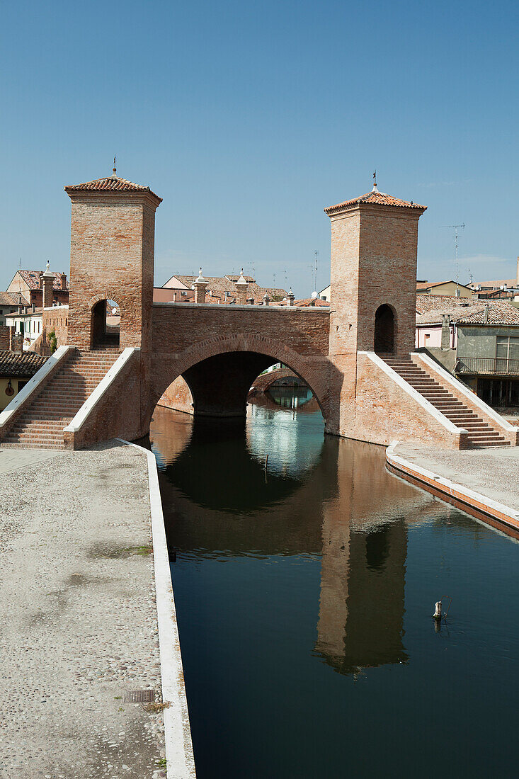 'Italy, Emilia-Romagna, Stone Bridge With Towers And Steps Reflecting In Water; Comacchio'