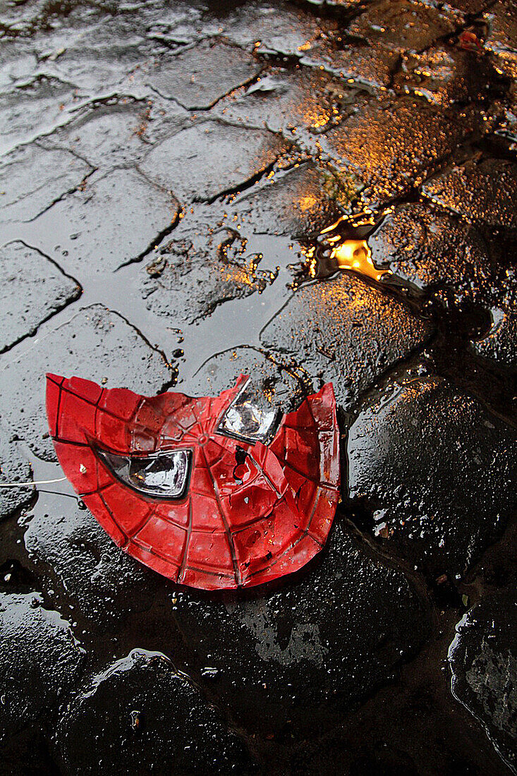 broken spiderman plastic mask on wet road in city town