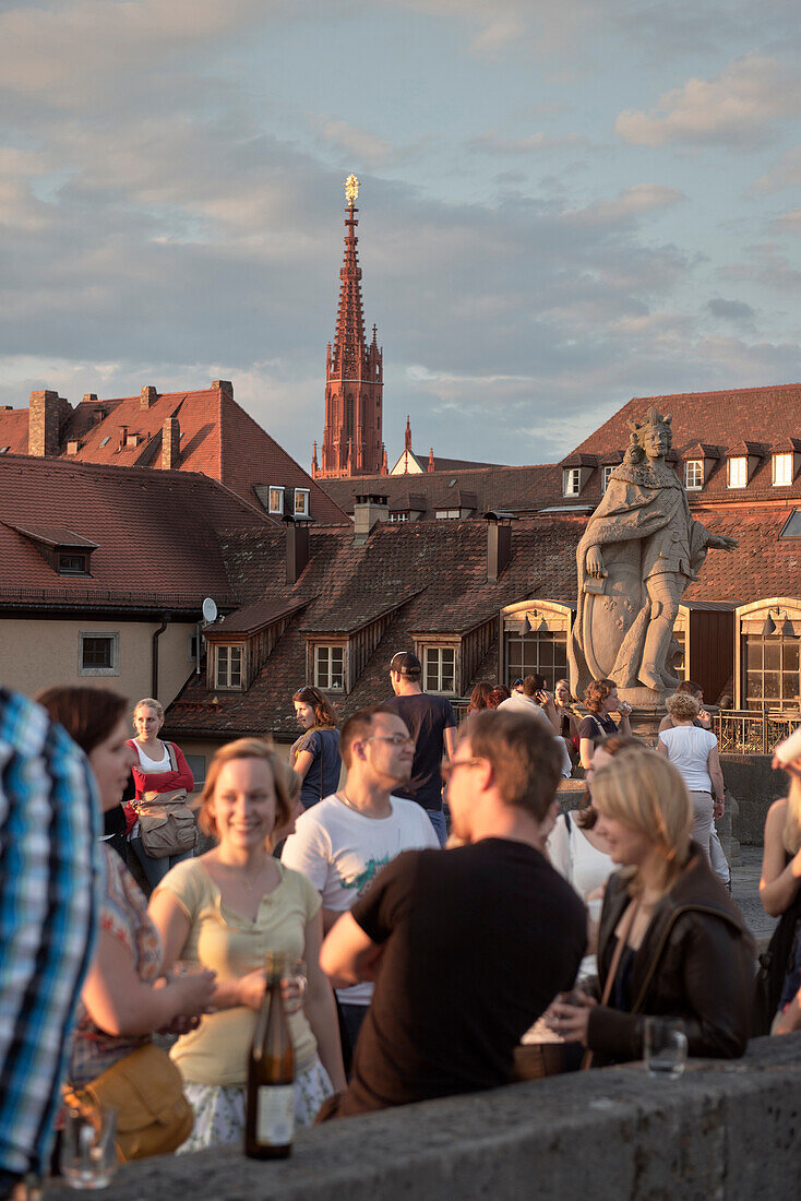 View across the old Main bridge to St. Mary's chapel, young people drinking wine at sunset, Wuerzburg, Franconia, Bavaria, Germany