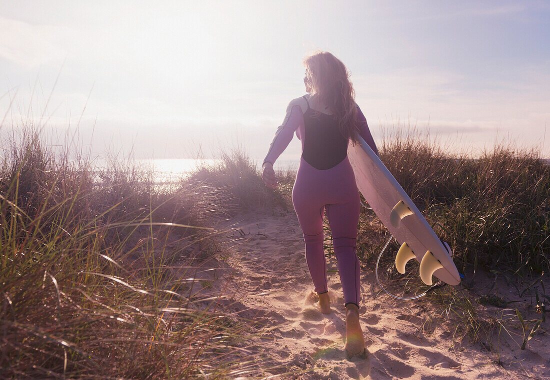 A woman carries her surfboard down a sandy path to the beach, Tarifa cadiz andaulsia spain