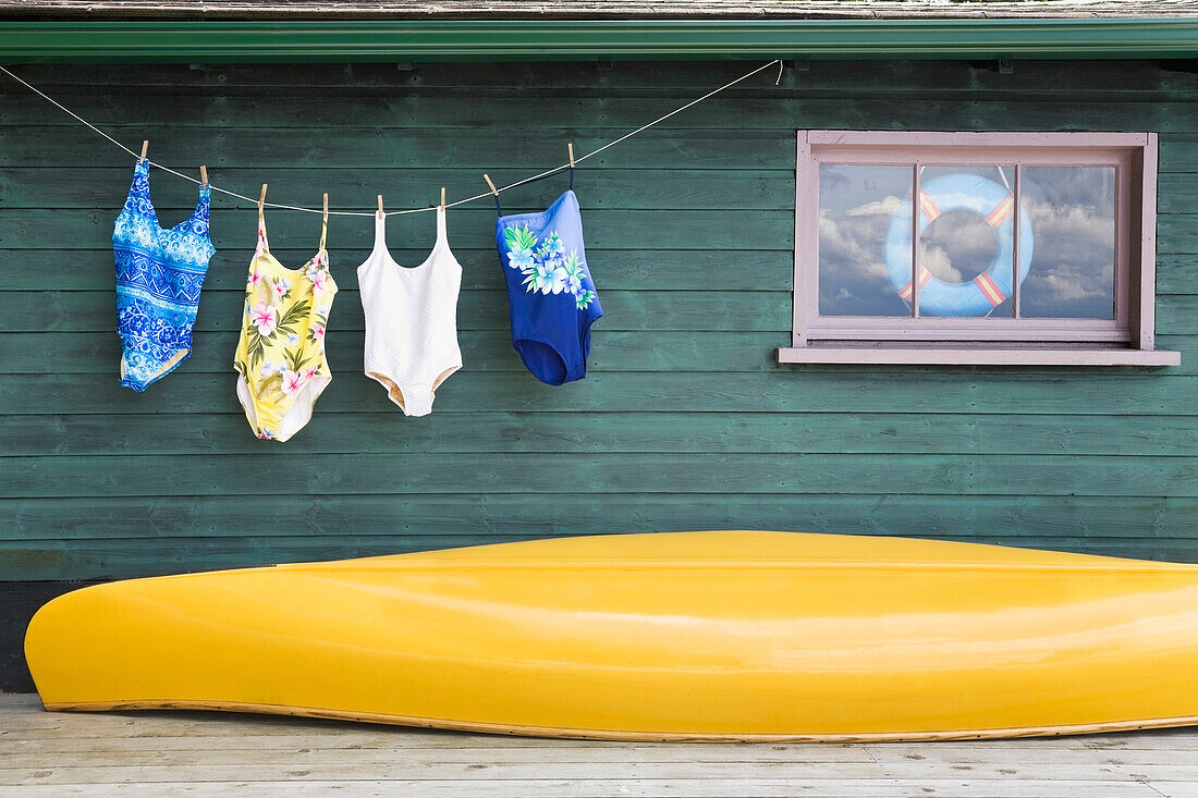 Bathing Suits On Clothes Line With Yellow Canoe Against Cottage, Ontario, Canada