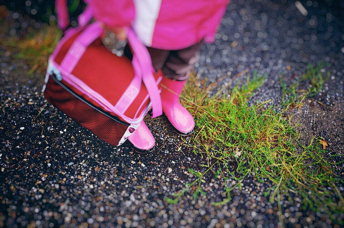Girl's Matching Pink Boots, Coat And Lunch Box On A Grassy Street