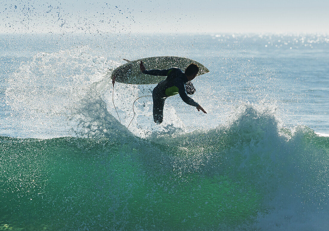Spain, Andalusia, Cadiz, Male surfer mid air in large splashing wave, Tarifa