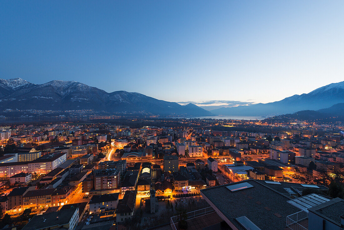 Lights illuminate the buildings at dusk and Lake Maggiore, Locarno, Ticino, Switzerland