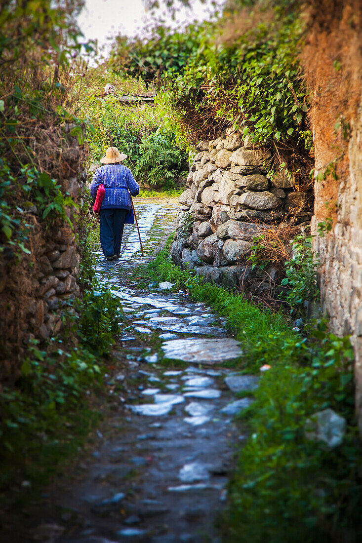 Old Chinese woman walks up winding stone path, Dali City, Yunnan, China