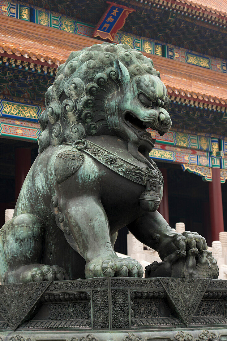 A lion statue in front of a building with colourful ornate facade at Forbidden City, Beijing, China