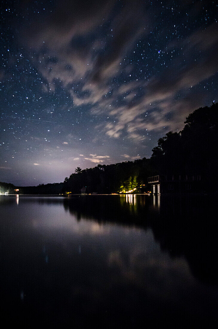 Stars in Cloudy Night Sky with Silhouetted Trees Reflecting in Lake
