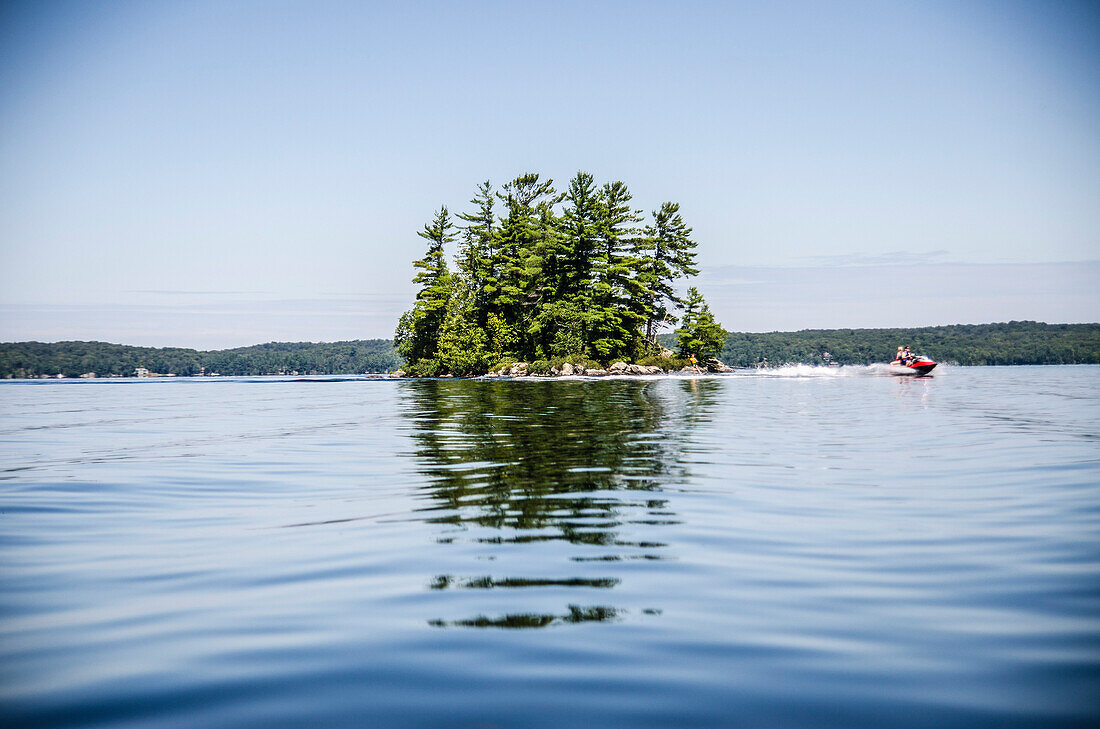 Jet Skier Passing Tree Covered Island Reflecting in Lake Water