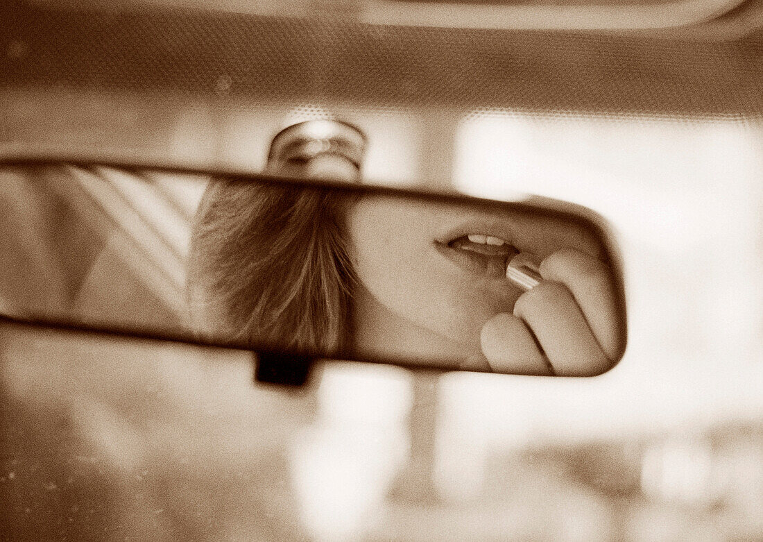 Junge Frau trägt Lippenstift auf und schaut in den Rückspiegel