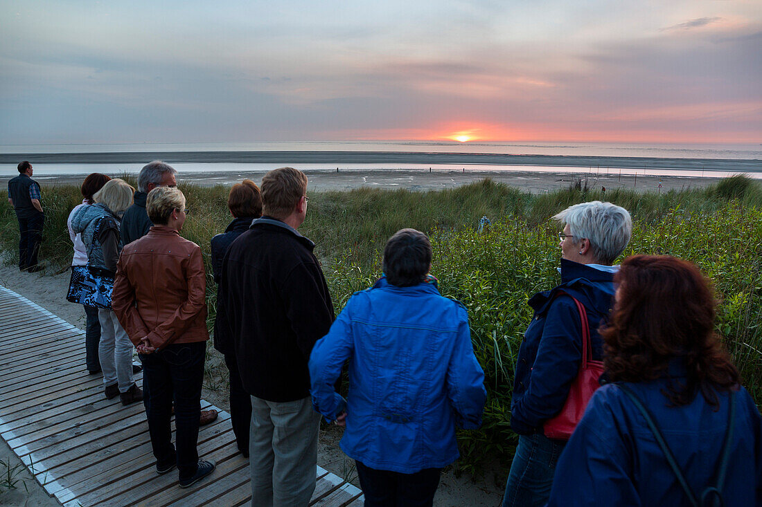 Touristen in Dünen am Strand beobachten den Sonnenuntergang, Langeoog, Ostfriesische Inseln, Nordsee, Ostfriesland, Niedersachsen, Deutschland, Europa