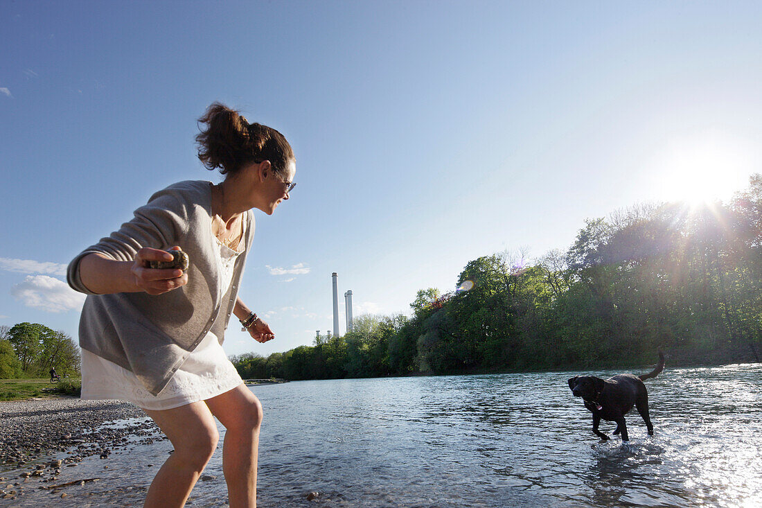 Woman playing with a dog at river Isar, Wittelsbach bridge, Munich, Bavaria, Germany