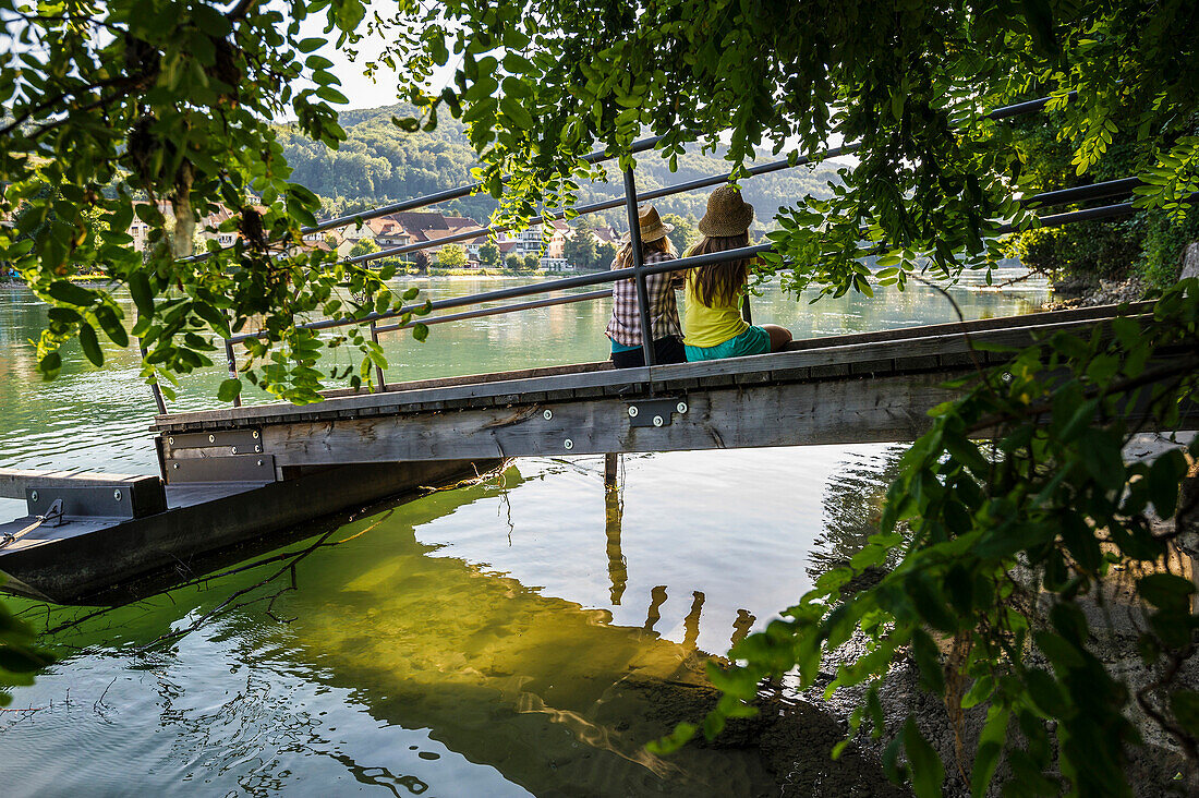 Zwei junge Frauen sitzen auf einem Steg am Rhein, Rheinfelden, Baden-Württemberg, Deutschland
