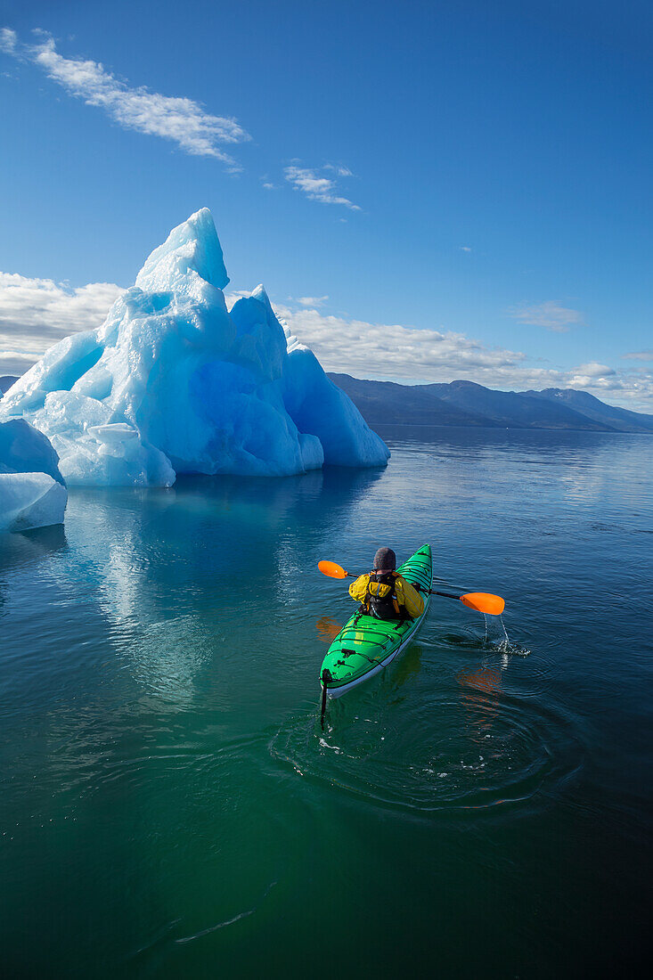 A sea kayaker paddles beside an iceberg in Southeast Alaska's Stephens Passage on a summer evening, Holkham Bay, Tracy Arm. MR_ Ed Emswiler, ID#12172012A