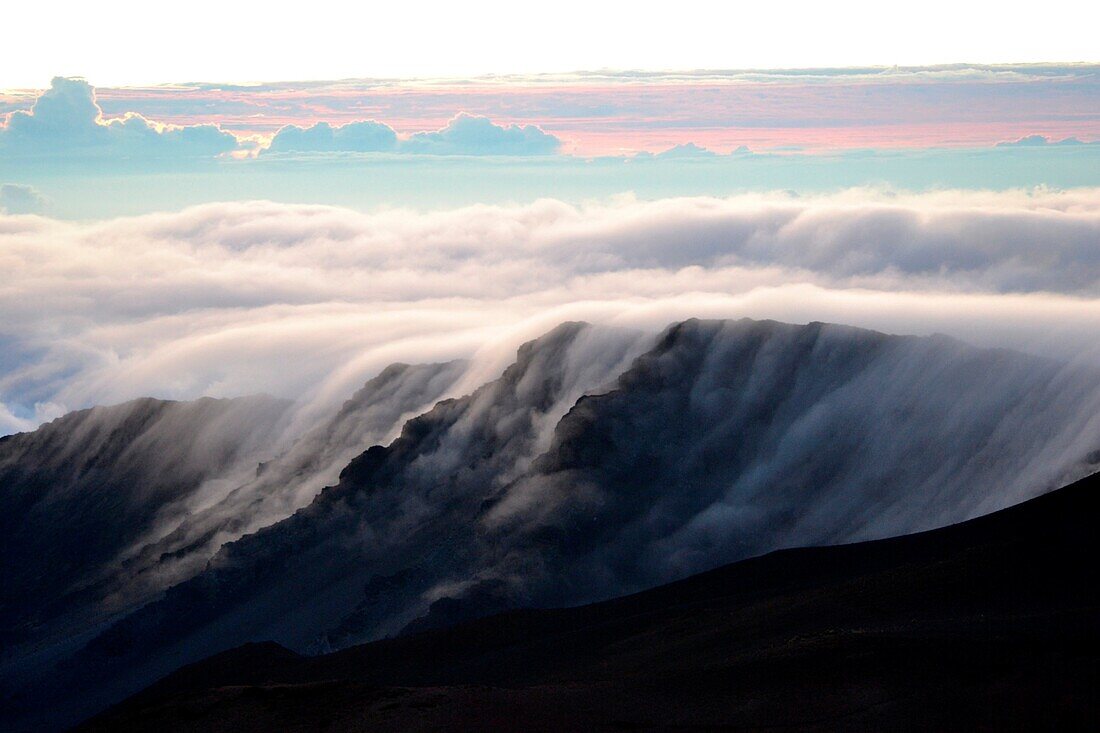 Clouds over a mountain edge at the summit of Haleakala volcana during sunrise, Maui, Hawaii, USA