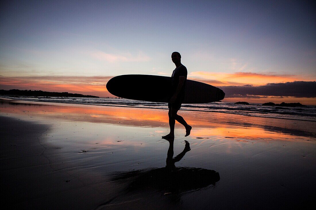 Silhouette of a man walking on a beach with surfboard during sunset, Costa Rica