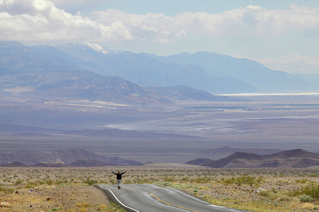 USA, Nevada border, California, Route 374, Death Valley National Park, Highway 374, Young woman standing on deserted road in desert
