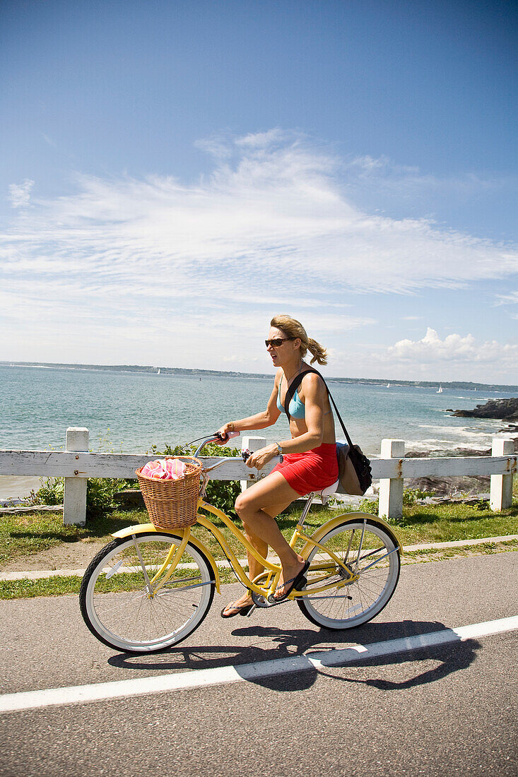 USA, Rhode Island, Young woman bicycling along Ocean Avenue, Newport