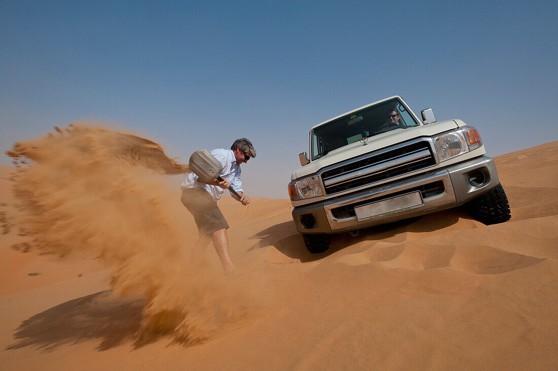 Man trying to dig out 4 wheel drive stuck in soft sand, Liwa, Abu Dhabi, UAE