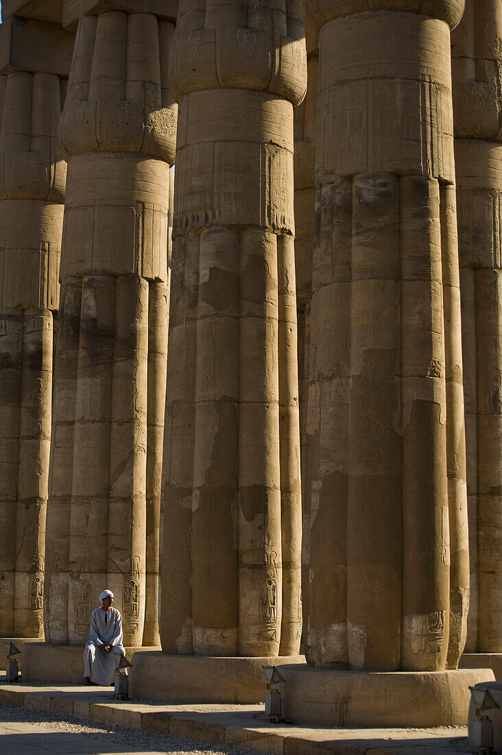 Temple guard sitting at base of papyrus-bundle columns with bud capitals in Court of Amenophis III, Luxor Temple, Luxor, Egypt